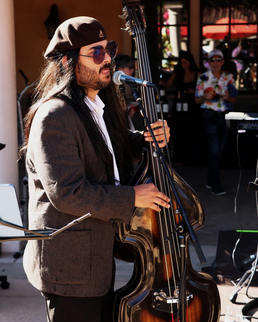 Hector Valencia in a beret, purple sunglasses and tweed jacket, singing as he plays his sunburst upright bass.