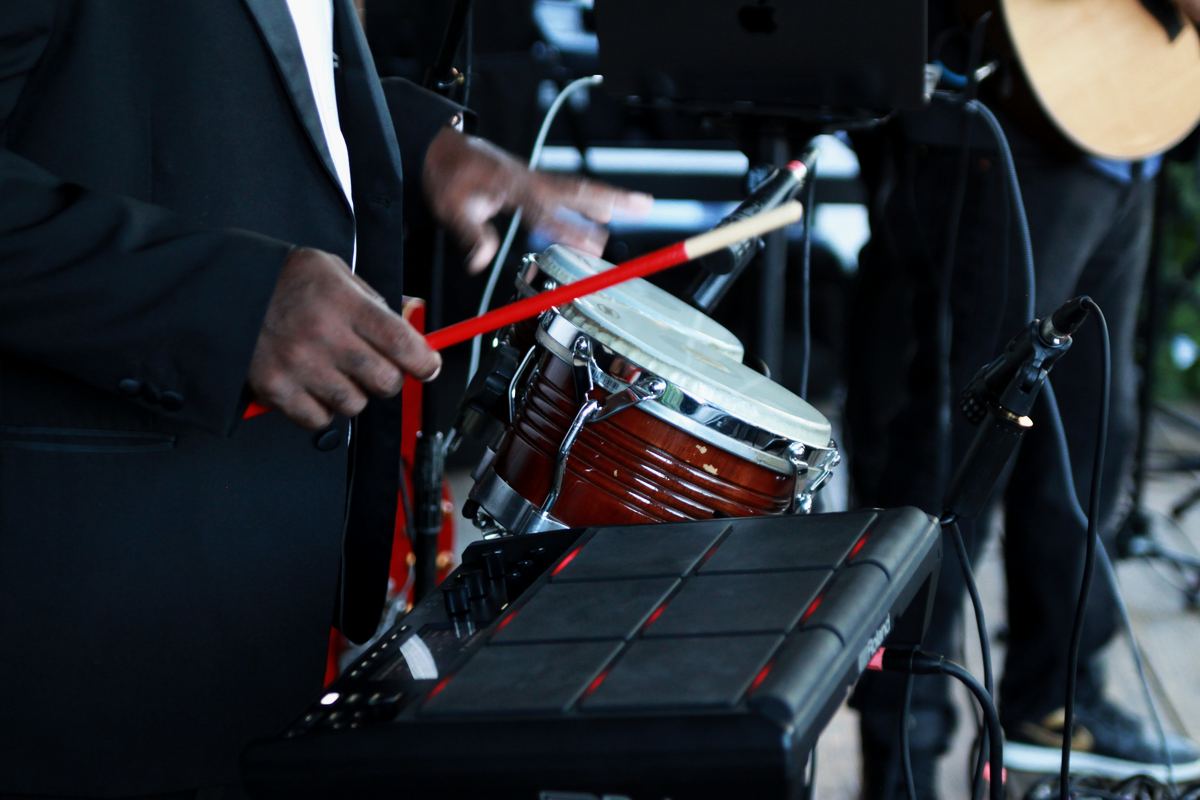 Close-up of hands playing a small drum with a red stick, next to a percussion pad.