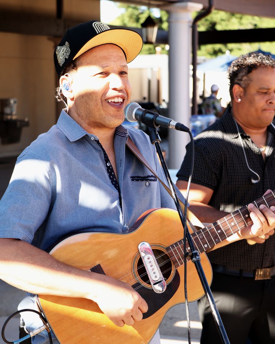 Jordan Wilson, Son Chévere's lead singer, laughing at the mic with his tres cubano, outdoors in the sun.